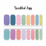 A mix of pastel solids covered with black speckled dots nail wrap nail design.  