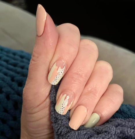 Combination of solid peach and solid pale green with accent nails that include strokes of peach, pale green and white with black dots nail wrap nail design